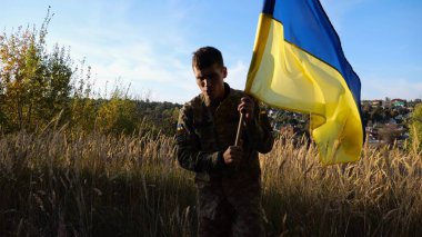 Üniformalı genç erkek asker Ukrayna bayrağıyla kırsalda yürüyor. Ukrayna ordusunun askeri ulusal pankartı kaldırıyor. Rus saldırganlığına karşı zafer.