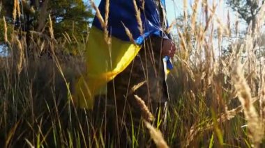 Ukraynalı asker kırsal kesimde mavi-sarı pankartıyla ayakta duruyor. Rus saldırısına karşı zafer sembolü olarak Ukrayna bayrağı taşıyan askeri üniformalı bir erkek asker. İstila direnişi.