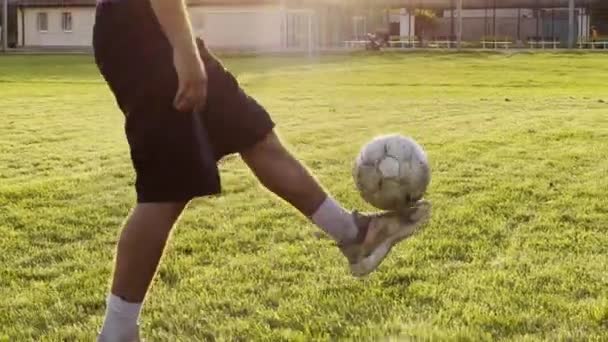 グリーンフィールドでボールを蹴るプロサッカー選手の男性フィート 日没のスタジアムでサッカーボールをジャグリングする若者の足 スポーツマンは屋外でトリックを練習します フリースタイルフットボール — ストック動画