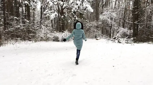 Young girl running on trail through snowy forest. Happy woman jogging on path at woodland. Cheerful lady having fun and enjoying winter time. Concept of a winter holiday.