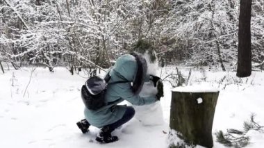 Kış ormanında kardan adam yapan mutlu kadın. Gülen kadın, Kardan Adam 'ı karlı parkta yaptıktan sonra kameraya bakıyor. Aktif ve eğlenceli vakit geçiren neşeli bir bayan. Kış tatili kavramı.