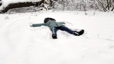 Ormandaki karlı çimlerde yatan ve melek yapan mutlu kadın. Genç kız karda oynuyor ve kışın tadını çıkarıyor. Neşeli bayan dışarıda eğleniyor. Kış tatili kavramı