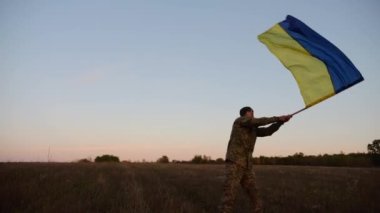 Ukrayna ordusunun genç askeri Rusya 'nın işgal ettiği özgür bölgede mavi-sarı bayrak sallıyor. Erkek ordu, hava kararırken Rus saldırısına karşı zafer onuruna Ukrayna bayrağını kaldırdı..