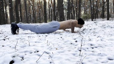 Güçlü bir adam kış ormanında karda şınav çekiyor. Sporcu doğada egzersiz yapıyor. Genç adam dışarıda antrenman yapıyor. Kas sporcusu sıkı ve yoğun idman yapıyor. Sportif yaşam tarzı kavramı.