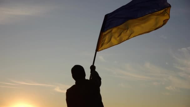 身穿军服的年轻人在美丽的夕阳西下挥舞着乌克兰国旗 男兵在农村升起了国旗 战胜俄罗斯侵略的胜利 — 图库视频影像