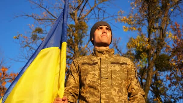 Український Військовий Стоїть Національним Прапором Сільській Місцевості Проти Блакитного Неба — стокове відео