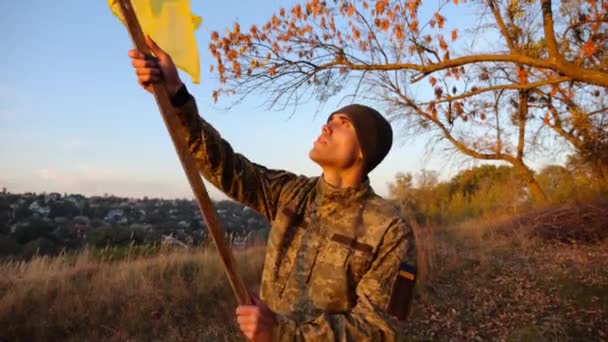 ウクライナの国旗を日没の丘の頂上に振るウクライナ軍の兵士 軍服の若者は田舎で国旗を掲揚した ロシア侵略に対する勝利 戦争の終わり — ストック動画