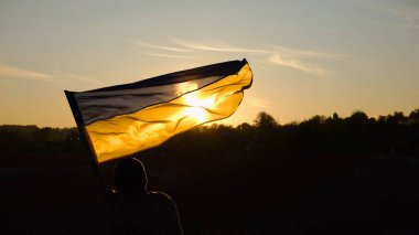 Askeri üniformalı genç adam arka planda güzel günbatımına karşı Ukrayna bayrağı sallıyor. Erkek Ukraynalı asker kırsal kesimde ulusal bayrağı kaldırdı. Rus saldırısına karşı zafer.
