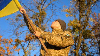 Kırsal kesimde Ukrayna bayrağı sallayan üniformalı bir erkek asker. Ukrayna ordusunun genç askeri Rus saldırısına karşı zafer sembolü olarak mavi-sarı bayrağı kaldırıyor. İstila direnişi kavramı.