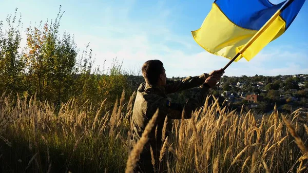 Kırsal kesimde Ukrayna bayrağı sallayan üniformalı bir erkek asker. Ukrayna ordusunun genç askeri Rus saldırısına karşı zafer sembolü olarak mavi-sarı bayrağı kaldırıyor. İstila direnişi kavramı