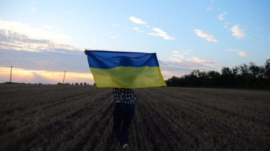 Ukraynalı kadın gün doğumunda ulusal mavi-sarı pankartıyla arpa çayırında yürüyor. Gün batımında başındaki buğday tarlasında Ukrayna bayrağını taşıyan bir kadın. Rus saldırısına karşı zafer