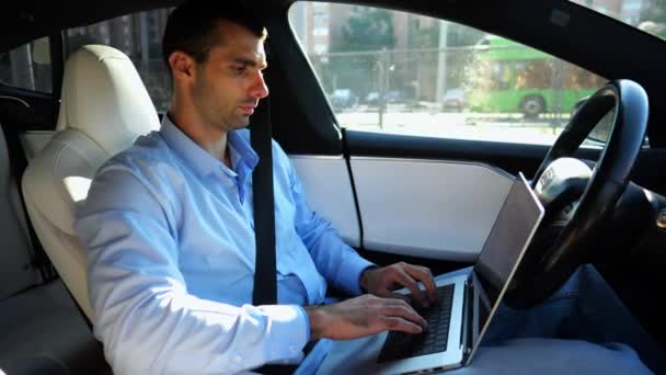 都市道路で自動運転する自動運転車に乗っている間 ノートブックに取り組むハンサムな起業家 オートパイロットで電気自動車に乗ってラップトップにテキストを入力する男性のビジネスマン — ストック動画