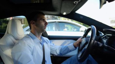 Şehir yolunda modern elektrikli araba kullanan yakışıklı bir işadamının profili. Erkek başarılı girişimci şehirde elektrikli araçla geziyor. Genç adam güneşli bir günde işe gidip geliyor. Yavaş çekim