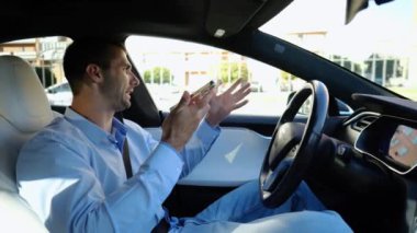 Erkek iş adamları, otomatik elektrikli araba kullanırken ciddi telefon konuşmaları yaparlar. Gergin iş adamı otomatik pilotla elektrikli otomobil kullanırken akıllı telefondan konuşur.
