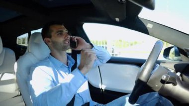 Şehir yolunda otomatik pilotla elektrikli otomobil sürerken akıllı telefondan konuşan erkek girişimci. Kendine güvenen işadamı, otomatik elektrikli araba kullanırken telefonla konuşuyor..