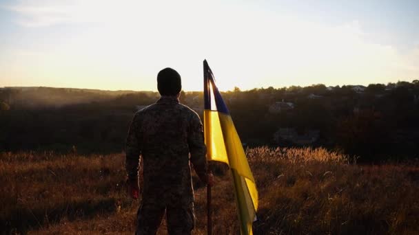 Ein Ukrainischer Armeeangehöriger Steht Bei Sonnenuntergang Mit Einer Nationalfahne Auf — Stockvideo