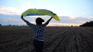 Ukraynalı kadın gün doğumunda ulusal mavi-sarı bayrak ile arpa çayırında koşuyor. Gün batımında kafasının üstünde Ukrayna bayrağıyla koşan bir kadın. Rus saldırısına karşı zafer.