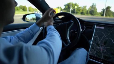 Şehirde elektrikli araba kullanırken direksiyonu işadamının elleri tutuyor. Şehir yolunda elektrikli araç kullanan bir erkek işadamı. Genç adam güneşli bir günde işe gidip geliyor.