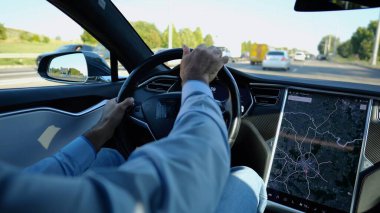 Şehirde elektrikli araba kullanırken direksiyonu işadamının elleri tutuyor. Şehir yolunda elektrikli araç kullanan bir erkek işadamı. Genç adam güneşli bir günde işe gidip geliyor.