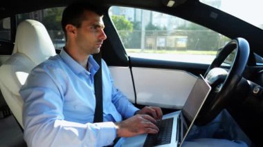 Şehir yolunda otonom bir otomatik araba sürerken dizüstü bilgisayar üzerinde çalışan yakışıklı bir girişimci. Erkek işadamı, otomatik pilotlu elektrikli aracın sürüşü sırasında dizüstü bilgisayarında yazı yazıyor..
