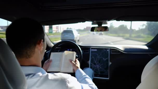 都市道路で自動操縦で電気自動車に乗っている間の男性ビジネスマン読書本 自動運転の電気自動車に乗っている間 彼の知識を向上させる成功したビジネスマン — ストック動画