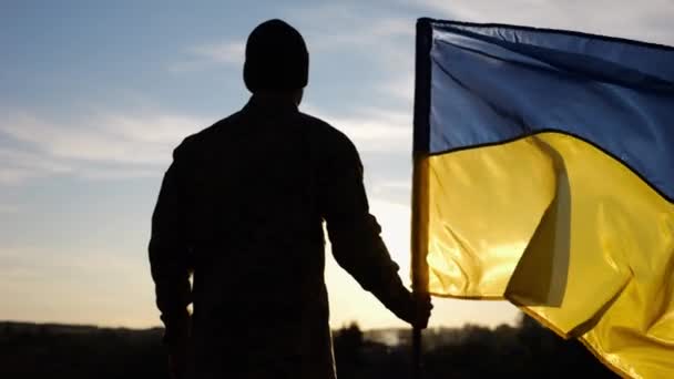 Ein Ukrainischer Armeeangehöriger Steht Bei Sonnenuntergang Mit Einer Nationalfahne Auf — Stockvideo