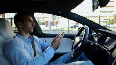 Erkek iş adamları, otomatik elektrikli araba kullanırken ciddi telefon konuşmaları yaparlar. Gergin iş adamı otomatik pilotla elektrikli otomobil kullanırken akıllı telefondan konuşur.