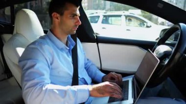 Şehir yolunda otonom bir otomatik araba sürerken dizüstü bilgisayar üzerinde çalışan yakışıklı bir girişimci. Erkek işadamı, otomatik pilotlu elektrikli aracın sürüşü sırasında dizüstü bilgisayarında yazı yazıyor..