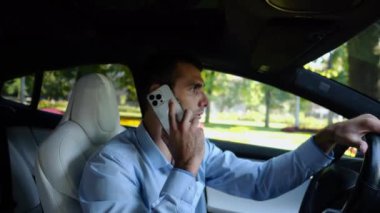 Şehir yolunda elektrikli araba kullanan ve telefonla konuşan kendine güvenen bir işadamı profili. Erkek iş adamı şehirde elektrikli araç kullanıyor ve akıllı telefondan konuşuyor. İş kavramı.