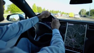 Şehirde elektrikli araba kullanırken direksiyonu işadamının elleri tutuyor. Şehir yolunda elektrikli araç kullanan bir erkek işadamı. Genç adam güneşli bir günde işe gidip geliyor.
