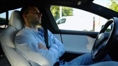 Kentsel yolda kendi kendini kullanan bir erkek işadamı deneyimi. Şehirdeki otomatik pilotla elektrikli otomobilde dinlenen kendine güvenen bir iş adamı. Yavaş çekim