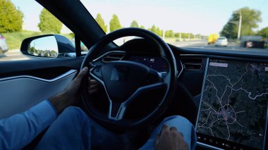 Şehirde elektrikli araba kullanırken direksiyonu işadamının elleri tutuyor. Şehir yolunda elektrikli araç kullanan bir erkek işadamı. Genç adam güneşli bir günde işe gidip geliyor.