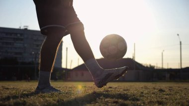 Yeşil sahada topa vuran genç adam bacakları. Günbatımında stadyumda futbol oynayan erkek futbolcu. Sporcu dışarıda numaralar yapıyor. Serbest stil futbol kavramı.