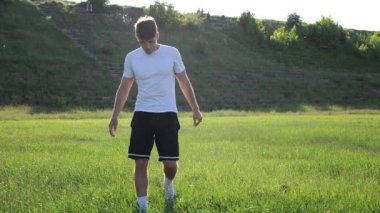 Profesyonel erkek futbolcu güneşli bir günde çayır boyunca yürüyor. Üniformalı genç yakışıklı sporcu başarılı bir maçtan sonra yeşil sahaya çıkıyor. Serbest stil futbol kavramı. Yavaş