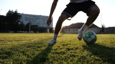 Profesyonel futbolcunun erkek ayağı, yeşil sahada koşarken topla numaralar gösterir. Sporcu bacakları gün batımında çayırda koşarken topa vurur. Stadyumda antrenman yapan genç adam. Yavaş çekim