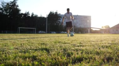 Sporcu gün batımında çayırda topa vuruyor. Yeşil sahada profesyonel futbolcu numaraları yapıyor. Stadyumda antrenman yapan genç adam. Serbest stil futbol kavramı. Yavaş çekim