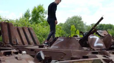 Rus ordusunun yok edilmiş askeri teçhizatına bakan genç adam. Ukrayna bölgesinde paslı ve yanmış zırhlı araçların sergilenmesi. Ukrayna ve Rusya arasındaki savaş. Yavaş çekim