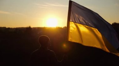 Erkek asker, güzel günbatımının arka planında Ukrayna bayrağıyla ayakta duruyor. Rus saldırısına karşı kazanılan zaferin şerefine mavi-sarı bayrak taşıyan Ukraynalı erkek asker..