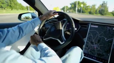Şehirde elektrikli araba kullanırken direksiyonu işadamının elleri tutuyor. Şehir yolunda elektrikli araç kullanan bir erkek işadamı. Genç adam güneşli bir günde işe gidip geliyor.