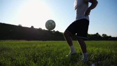 Güneşli bir günde stadyumda futbol topuyla hokkabazlık yapan sporcu. Genç adam yeşil sahada topa vuruyor. Profesyonel futbolcu, arka planda güneş ışığıyla çayırda numaralar yapıyor. Serbest stil futbol.