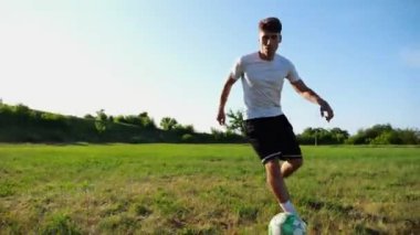 Üniformalı profesyonel futbolcu yeşil sahada koşarken topa numara yapıyor. Sporcu güneşli bir günde Meadow 'da koşarken topa vurur. Stadyumda antrenman yapan genç adam. Serbest stil futbol.