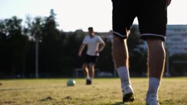 Günbatımında stadyumda futbol topu atan profesyonel futbolcuların erkek ayakları. Yeşil sahada topa vuran sporcu bacakları. Genç adamlar Meadow 'da antrenman yapıyor. Serbest stil futbol kavramı. Yavaş