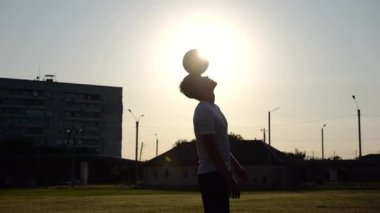 Sporcunun silueti gün batımında sahada topla numara yapıyor. Çayır 'da üniformalı profesyonel erkek futbolcu. Arka planda güneş ışığı var. Serbest stil futbol kavramı.