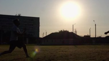 Günbatımında stadyumda futbol oynayan profesyonel futbolcuların silueti. Sahada birbirlerine pas verirken iki sporcu topla numara yapıyor. Serbest stil futbol.