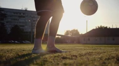 Yeşil sahada topa vuran genç adam bacakları. Günbatımında stadyumda futbol oynayan erkek futbolcu. Sporcu dışarıda numaralar yapıyor. Serbest stil futbol kavramı.