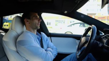 Kentsel yolda kendi kendini kullanan bir erkek işadamı deneyimi. Şehirdeki otomatik pilotla elektrikli otomobilde dinlenen kendine güvenen bir iş adamı. Yavaş çekim