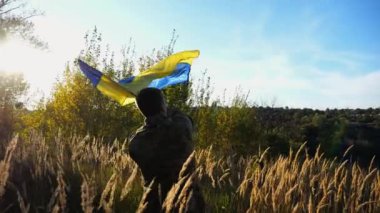 Kırsal kesimde Ukrayna bayrağı sallayan üniformalı bir erkek asker. Ukrayna ordusunun genç askeri Rus saldırısına karşı zafer sembolü olarak mavi-sarı bayrağı kaldırıyor. İstila direnişi kavramı.