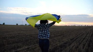 Ukraynalı bir kadın gün batımında kafasının üstünde Ukrayna bayrağıyla koşuyor. Bayan gün doğumunda ulusal mavi-sarı bayrak ile arpa çayırında koşuyor. Rus saldırısına karşı zafer.