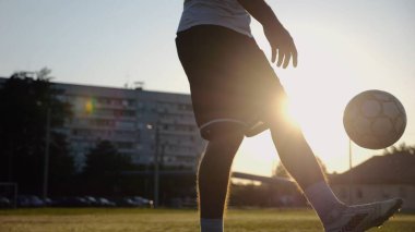 Yeşil sahada topa vuran genç adam bacakları. Günbatımında stadyumda futbol oynayan erkek futbolcu. Sporcu dışarıda numaralar yapıyor. Serbest stil futbol kavramı.