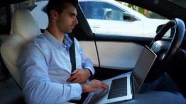 Şehir yolunda otonom bir otomatik araba sürerken dizüstü bilgisayar üzerinde çalışan yakışıklı bir girişimci. Erkek işadamı, otomatik pilotlu elektrikli aracın sürüşü sırasında dizüstü bilgisayarında yazı yazıyor..
